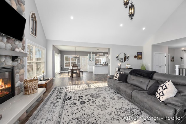 living area with high vaulted ceiling, a stone fireplace, wood finished floors, and an inviting chandelier