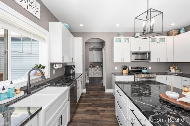 kitchen with arched walkways, glass insert cabinets, appliances with stainless steel finishes, dark wood-style flooring, and a sink