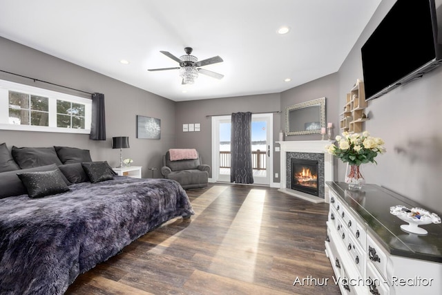 bedroom with access to outside, dark wood-style flooring, a glass covered fireplace, and recessed lighting