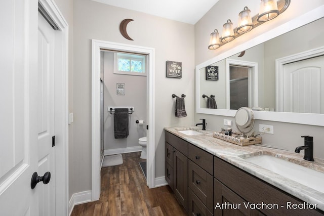 full bath with double vanity, a sink, toilet, and wood finished floors