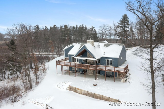 snow covered property featuring stone siding, a chimney, and a wooden deck