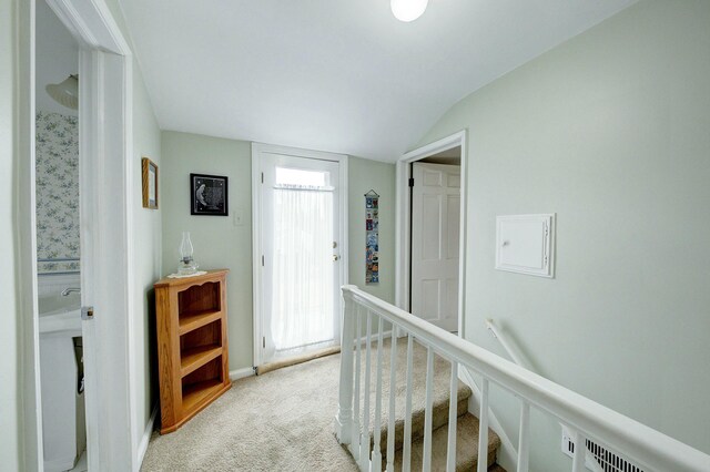 hallway with vaulted ceiling, an upstairs landing, and light colored carpet