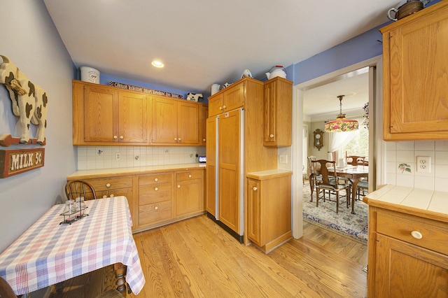 kitchen featuring tile counters, recessed lighting, light wood-style flooring, decorative backsplash, and paneled refrigerator