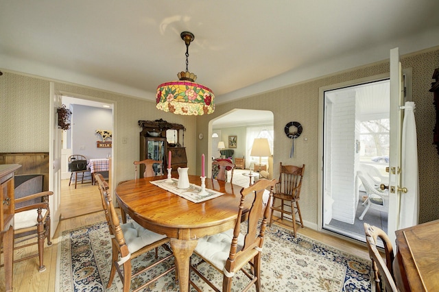 dining space featuring plenty of natural light, wallpapered walls, light wood-style flooring, and arched walkways