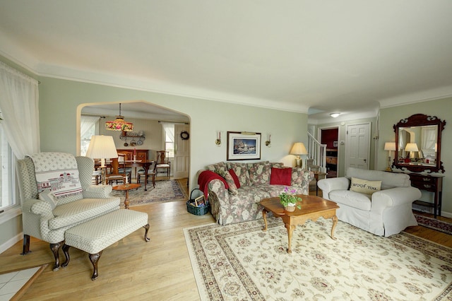 living area featuring light wood-style floors, arched walkways, ornamental molding, and stairway