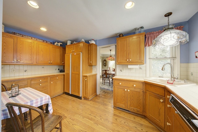 kitchen with light wood-style floors, a sink, tile counters, and paneled appliances