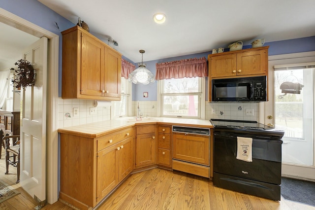 kitchen featuring a sink, tile counters, decorative backsplash, black appliances, and light wood finished floors