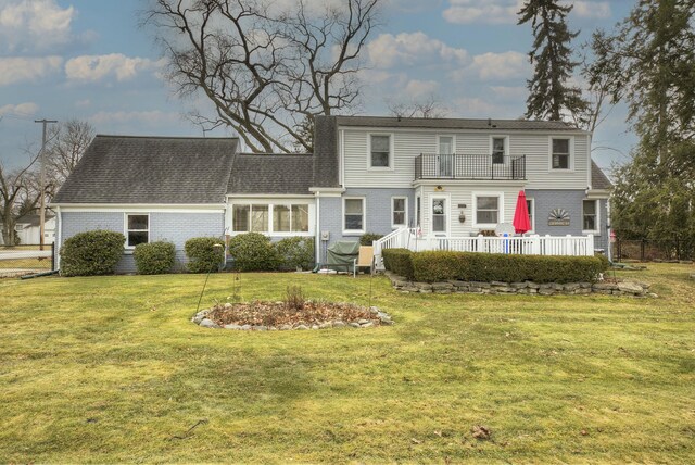 view of front of home featuring a balcony, a shingled roof, a front lawn, and brick siding