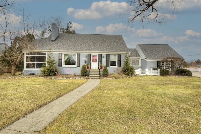 view of front of property featuring a shingled roof, brick siding, fence, a front lawn, and a chimney