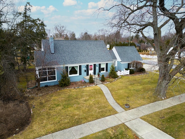 cape cod home with roof with shingles, a chimney, and a front yard