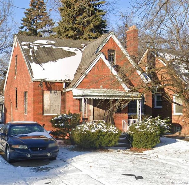 view of front of home with covered porch, brick siding, and a chimney