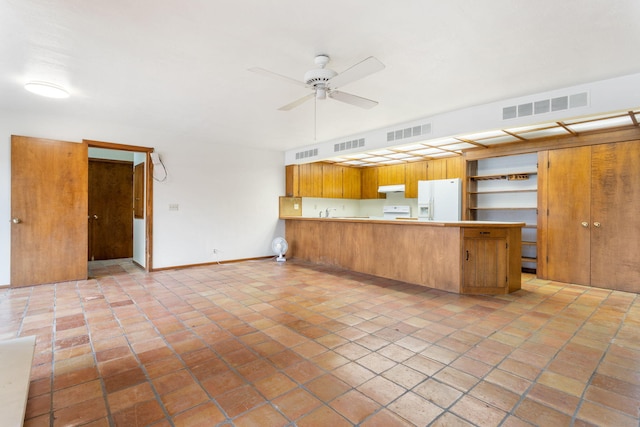 kitchen with under cabinet range hood, visible vents, white fridge with ice dispenser, and a peninsula