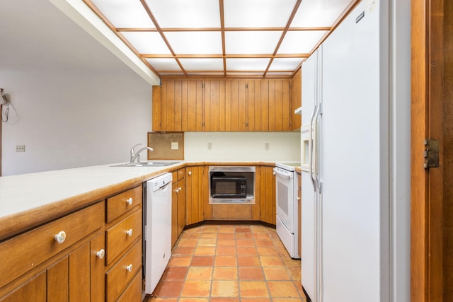 kitchen with brown cabinetry, white appliances, light countertops, and a sink