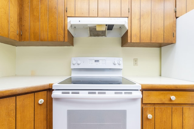 kitchen featuring white electric range, brown cabinets, under cabinet range hood, and light countertops