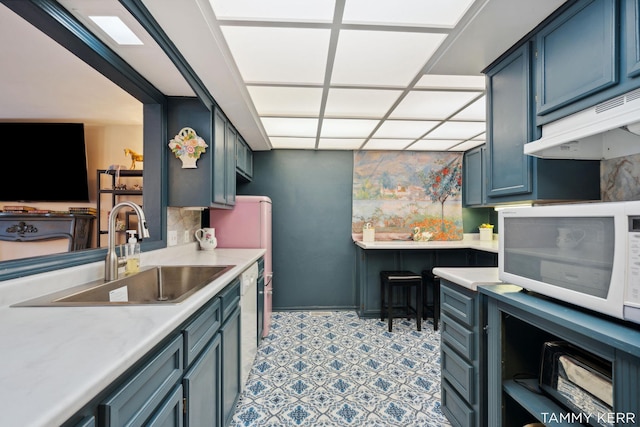 kitchen with a drop ceiling, white microwave, light countertops, under cabinet range hood, and a sink