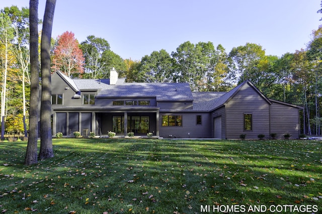 back of property with a sunroom, a lawn, a chimney, and an attached garage