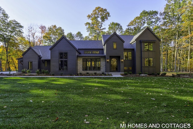 view of front of property with a front yard, stone siding, and roof with shingles