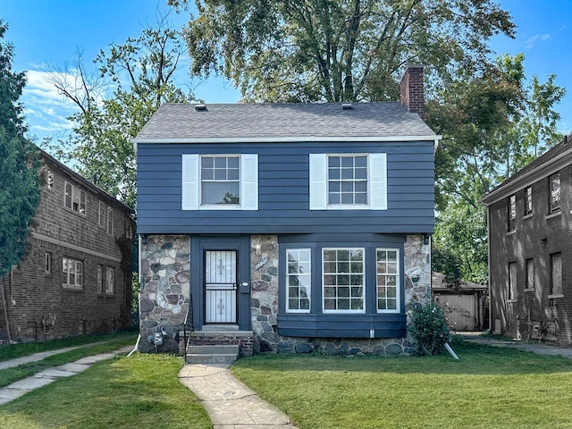 colonial house with stone siding, a front lawn, a chimney, and a shingled roof