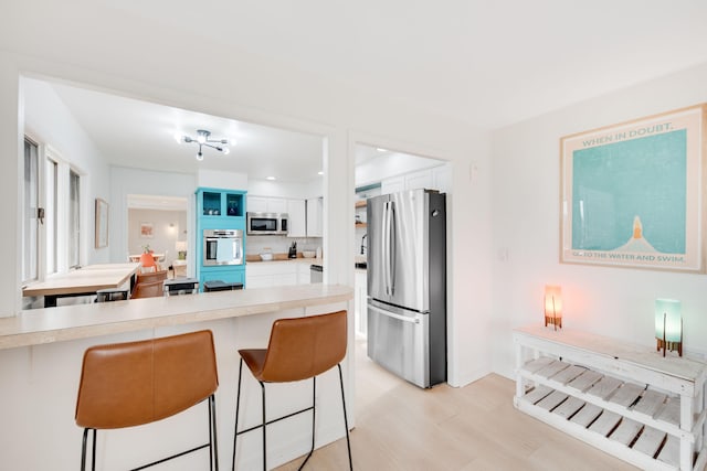 kitchen featuring light wood finished floors, a breakfast bar area, stainless steel appliances, light countertops, and white cabinetry