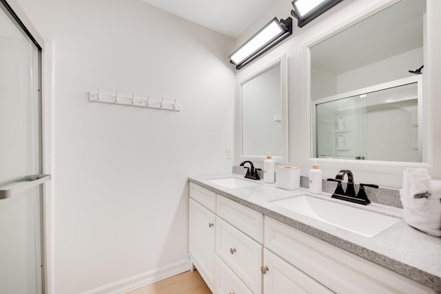 bathroom featuring double vanity, a stall shower, a sink, and wood finished floors