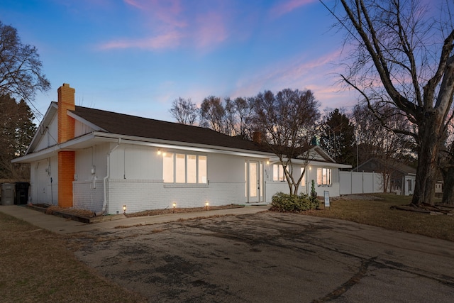 view of front of house with brick siding, a chimney, an attached garage, and fence