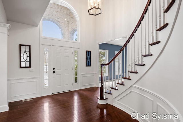 entrance foyer featuring a chandelier, a decorative wall, a towering ceiling, and hardwood / wood-style floors