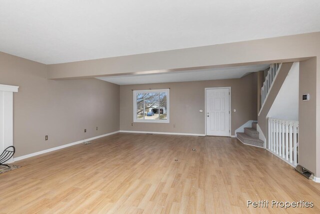 unfurnished living room with light wood-style floors, baseboards, and stairway