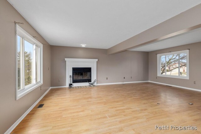 unfurnished living room with light wood-type flooring, a fireplace with flush hearth, visible vents, and baseboards