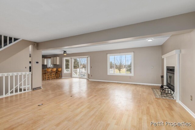 unfurnished living room featuring a fireplace with flush hearth, light wood-style flooring, and baseboards