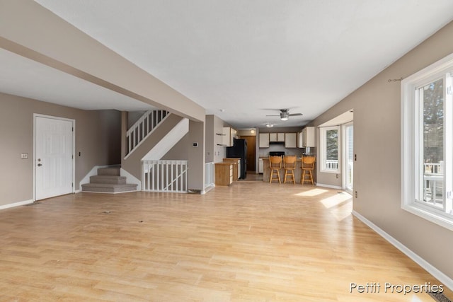 unfurnished living room featuring stairs, ceiling fan, light wood-style flooring, and baseboards