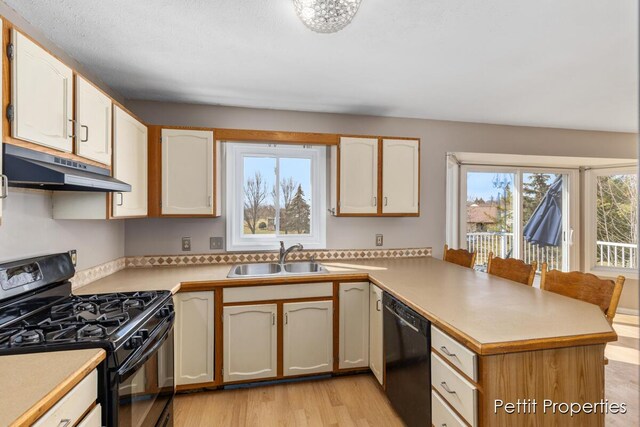 kitchen featuring light countertops, a sink, a peninsula, under cabinet range hood, and black appliances