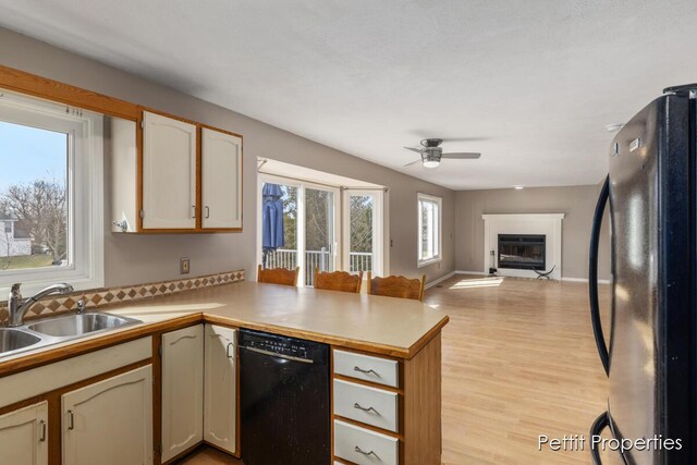 kitchen featuring a glass covered fireplace, open floor plan, a sink, a peninsula, and black appliances