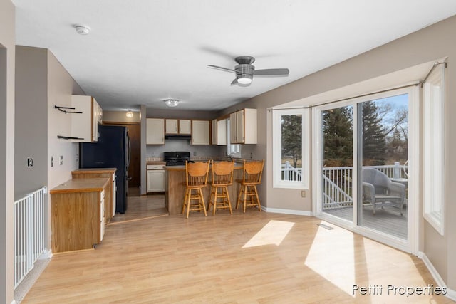 kitchen with a peninsula, black appliances, light wood-style flooring, and a kitchen bar