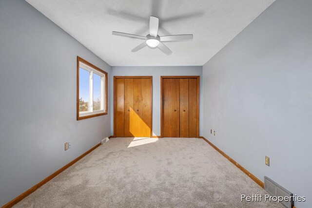 unfurnished bedroom with carpet floors, visible vents, baseboards, and two closets