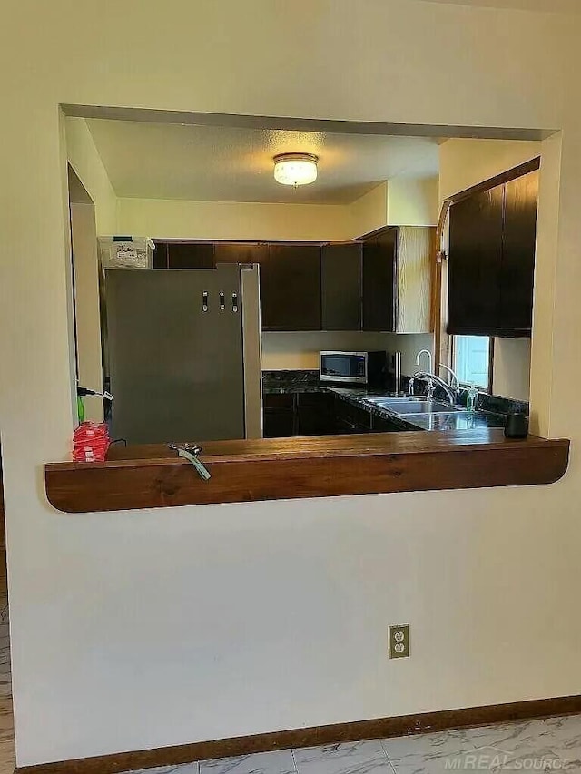 kitchen with appliances with stainless steel finishes, butcher block counters, a sink, and baseboards