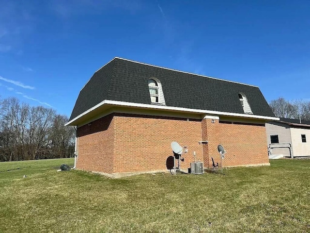 view of home's exterior featuring roof with shingles, brick siding, a lawn, and mansard roof