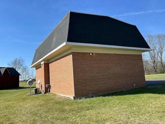 view of side of home featuring roof with shingles, brick siding, a yard, mansard roof, and central air condition unit