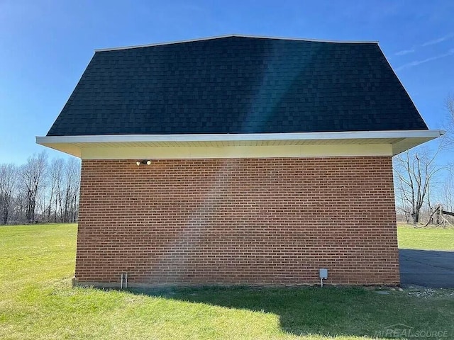 view of side of property with brick siding, roof with shingles, and a lawn