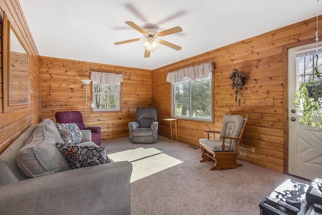 living area with carpet flooring, ceiling fan, and wooden walls