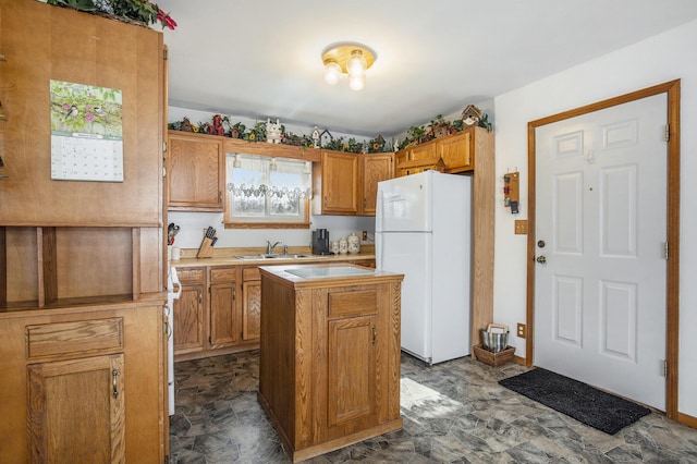 kitchen featuring a sink, light countertops, freestanding refrigerator, a center island, and brown cabinetry