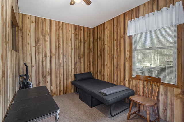 sitting room with a ceiling fan, carpet, and wood walls