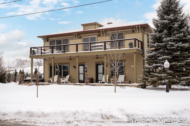 snow covered back of property with ceiling fan and a balcony