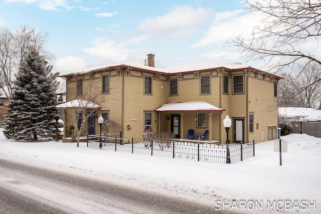 snow covered house with fence and a chimney