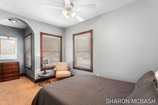 bedroom featuring a ceiling fan, light colored carpet, arched walkways, and baseboards