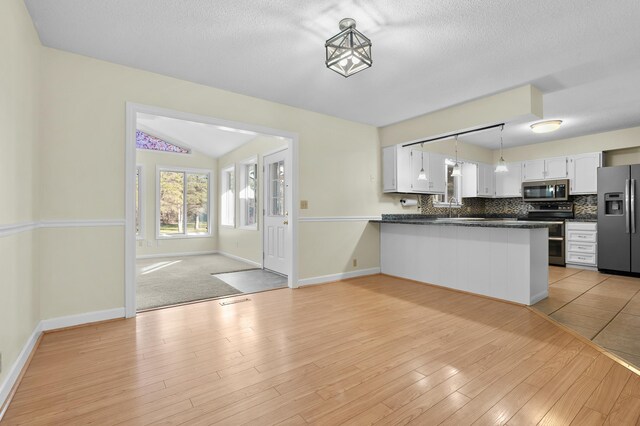 kitchen with decorative backsplash, dark countertops, a peninsula, stainless steel appliances, and white cabinetry