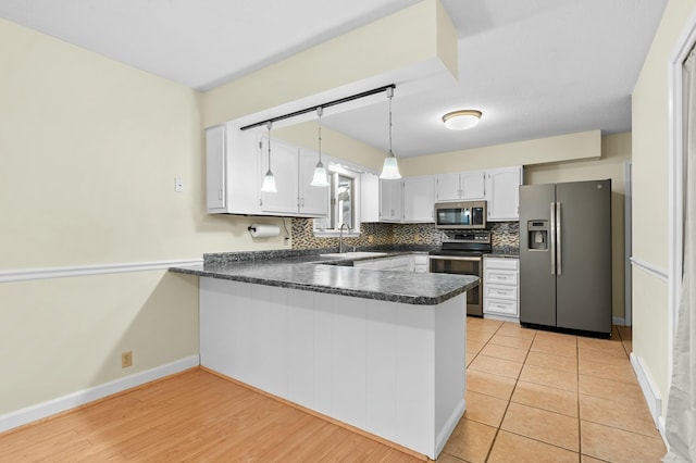 kitchen with decorative backsplash, dark countertops, a peninsula, stainless steel appliances, and a sink