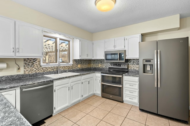 kitchen with light tile patterned floors, a sink, white cabinets, appliances with stainless steel finishes, and dark countertops