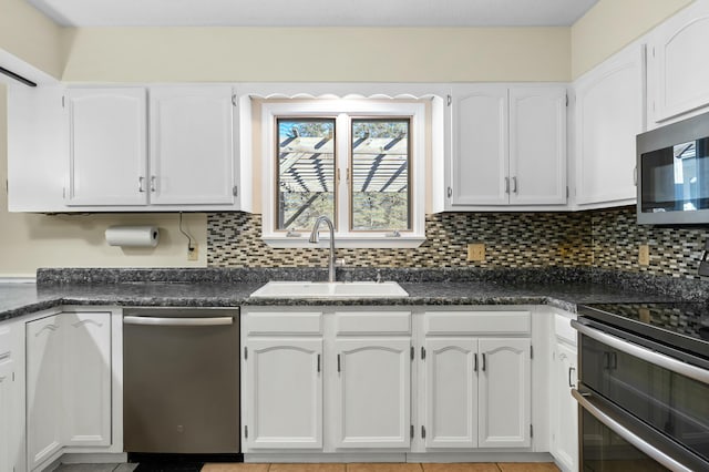 kitchen with stainless steel appliances, a sink, white cabinetry, decorative backsplash, and dark countertops