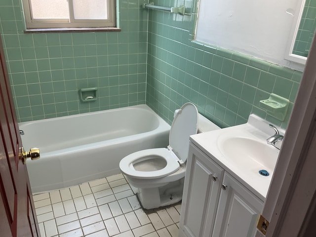 bathroom with toilet, tile patterned floors, vanity, tile walls, and shower / bathing tub combination