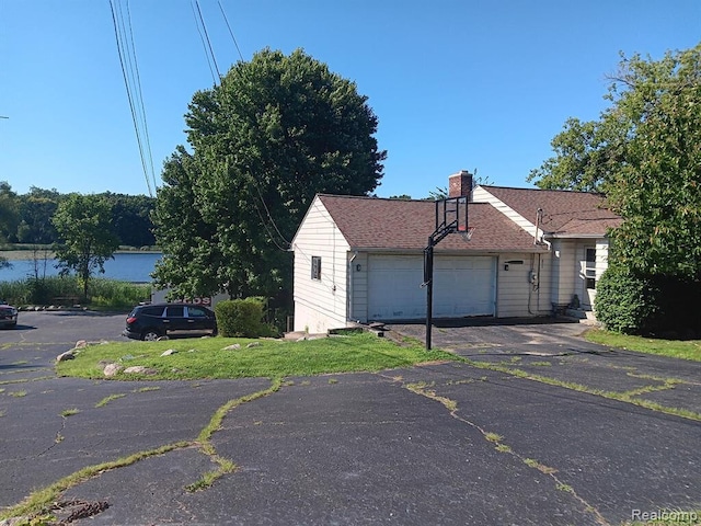 view of front of home featuring an attached garage, a chimney, aphalt driveway, and roof with shingles